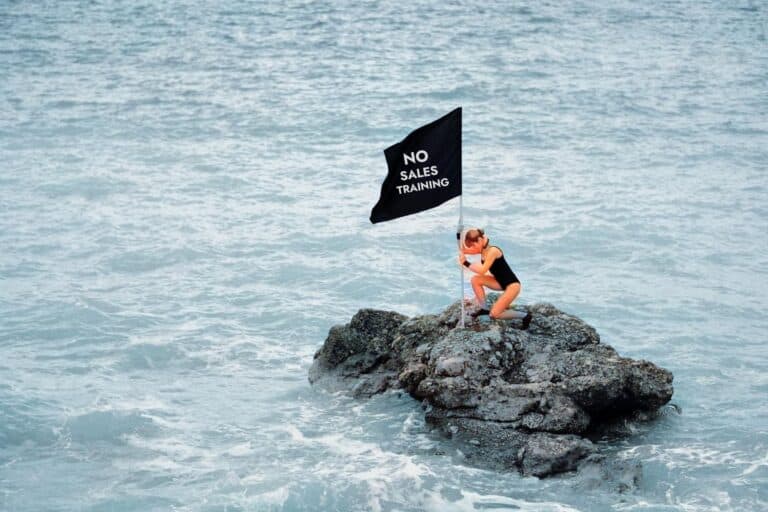woman on rock in ocean placing a flag stating no sales training needed